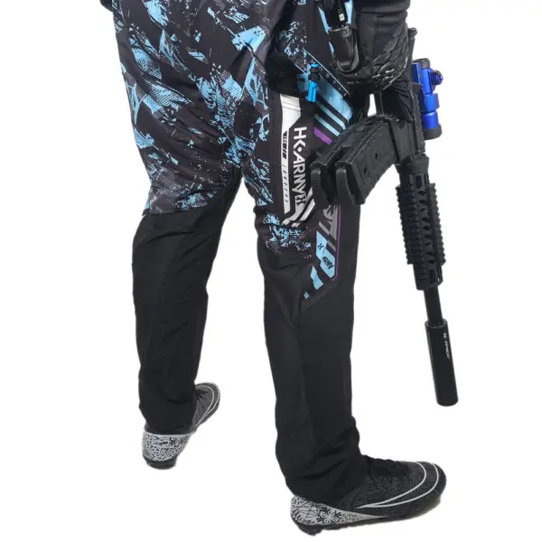 Person in paintball pants holding a paintball gun.